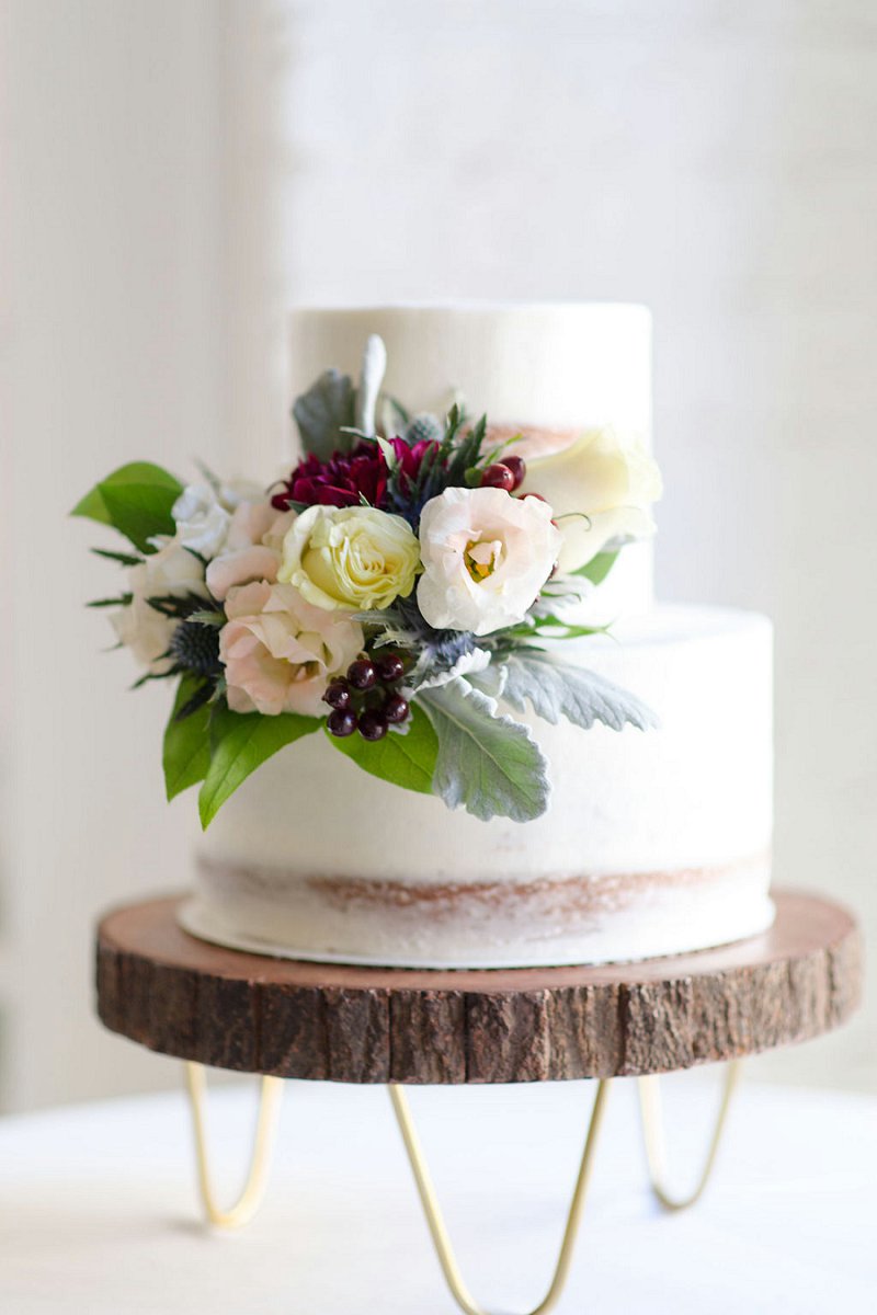 Sweet petite two tiered semi naked wedding cake on a modern wood slab cake stand for winter wedding