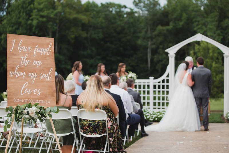 Outdoor rustic wedding ceremony with Song of Solomon Bible verse for a wedding welcome sign