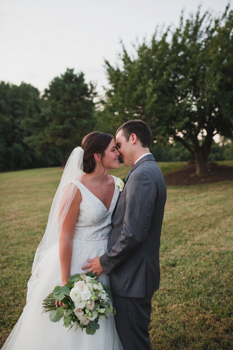 Bride in a sleeveless wedding dress with a lace bodice and tulle skirt standing next to her groom in a gray suit