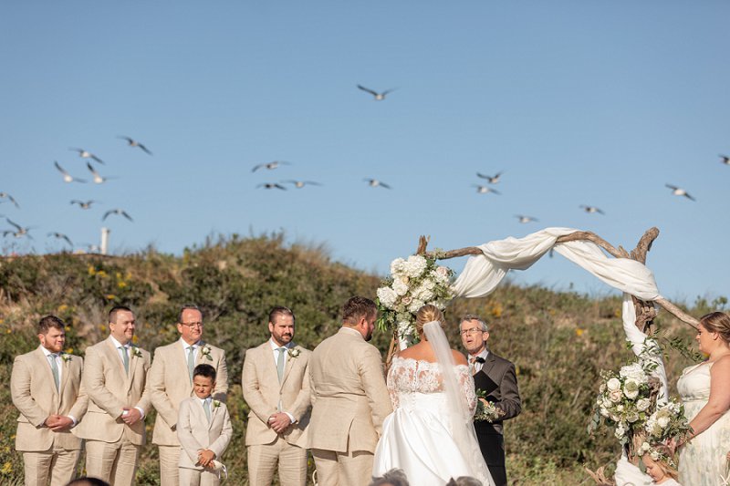 Romantic beachside wedding ceremony at Sanderling Resort in Outer Banks with driftwood ceremony arch and white drapery