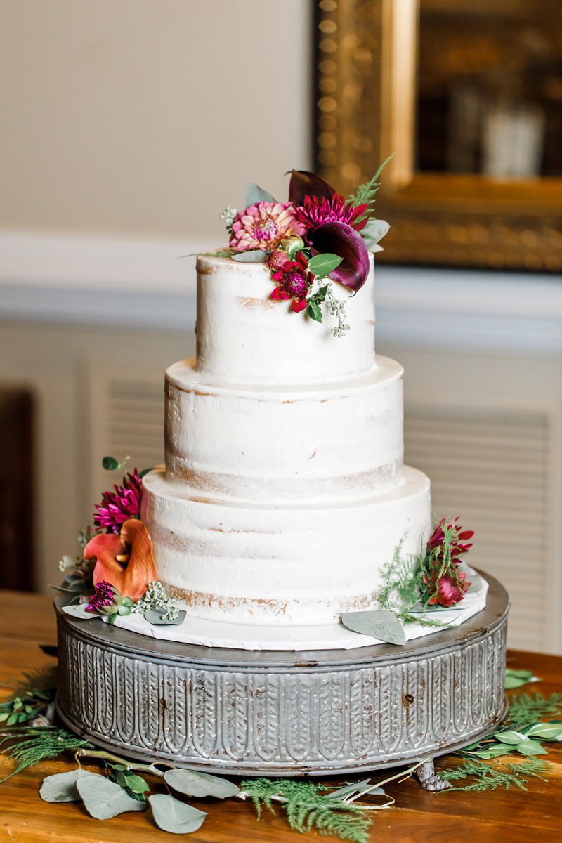 White three tiered almond chiffon wedding cake with whipped almond custard and raspberry preserves decorated with fall colored wedding flowers