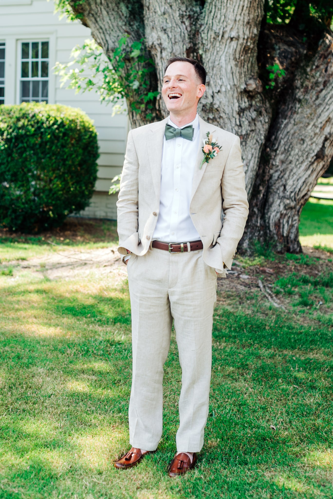 Groom wearing a tan linen suit with a dark green bow tie and brown loafers