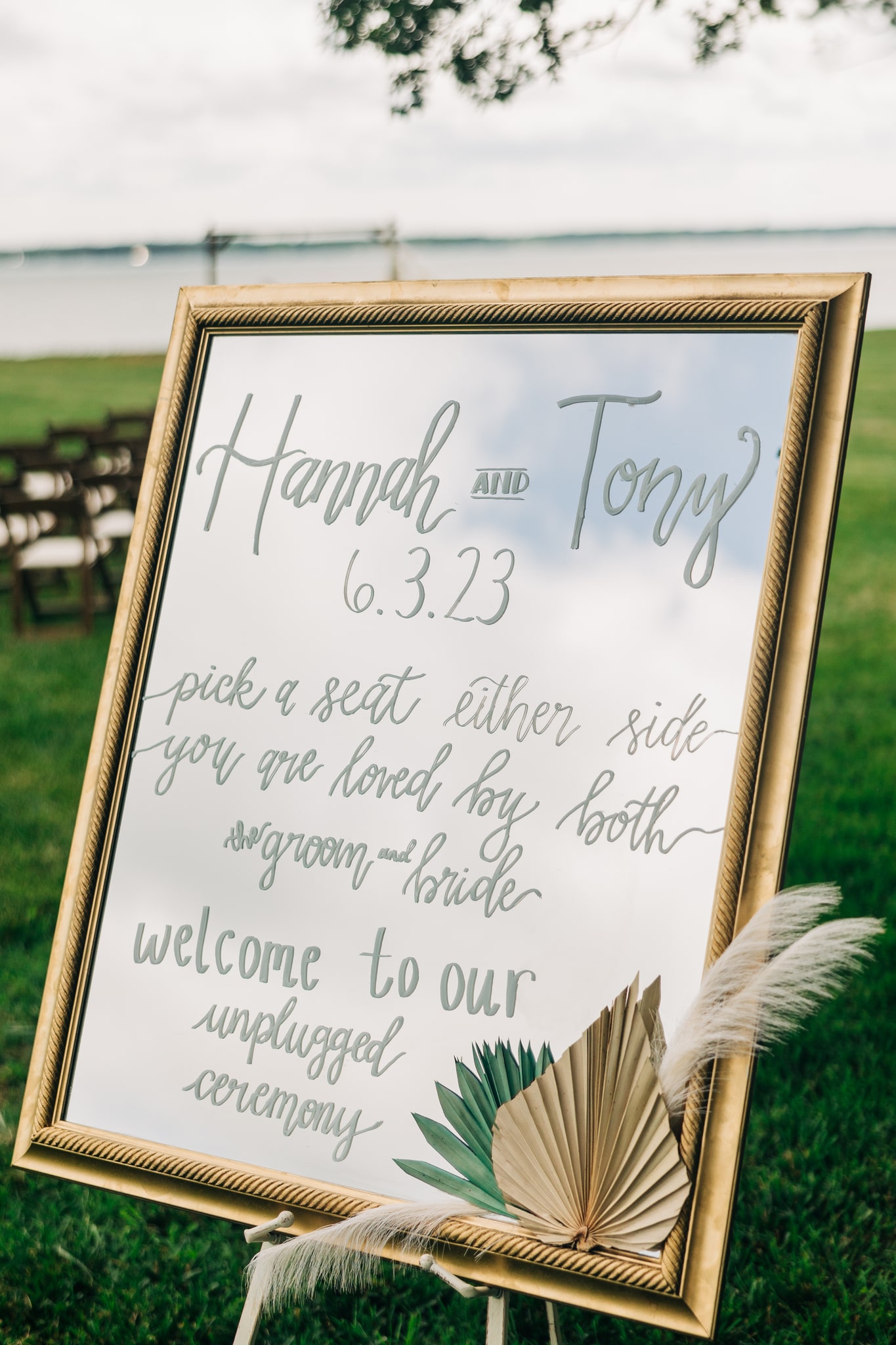 Unplugged wedding ceremony sign on a mirror with white calligraphy and pampas grass