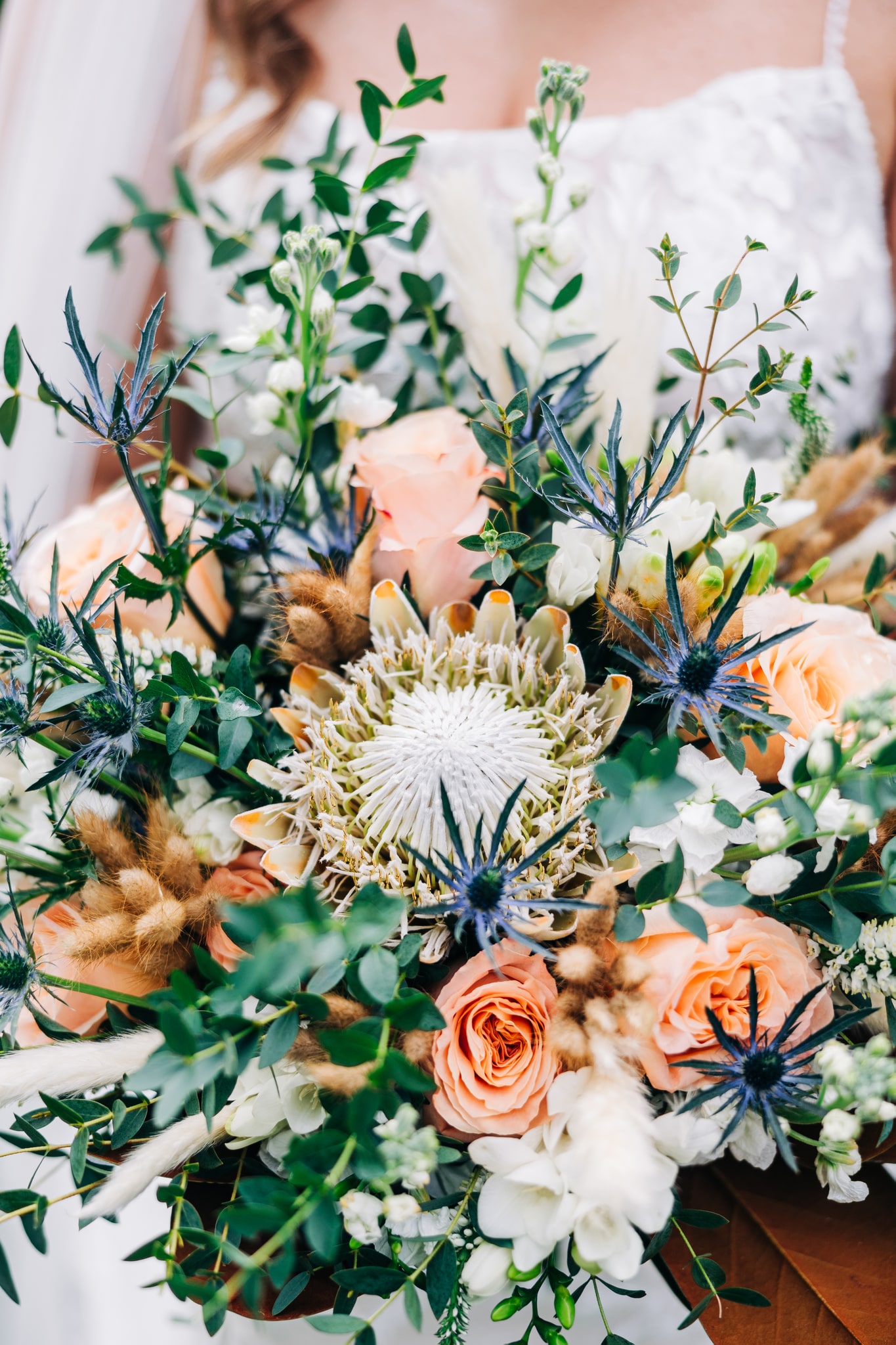 Lush wedding bouquet with king protea flower and blue thistle for a rustic bride